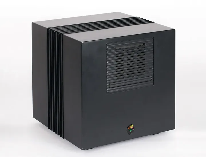 A black cube-shaped NeXTcube computer with vertical ribbed fins along one side, a recessed disc-drive panel on the front, and a small NeXT logo near the bottom edge.